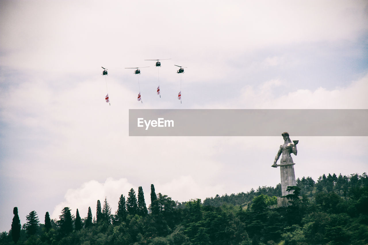 Low angle view of helicopters flying with flags by statue against sky