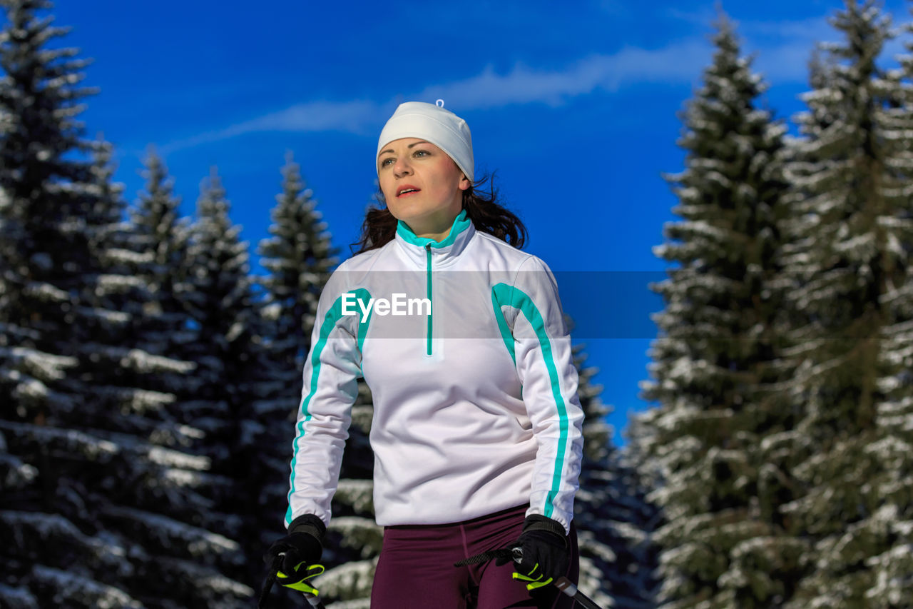 Low angle view of mid adult woman skiing against trees in forest