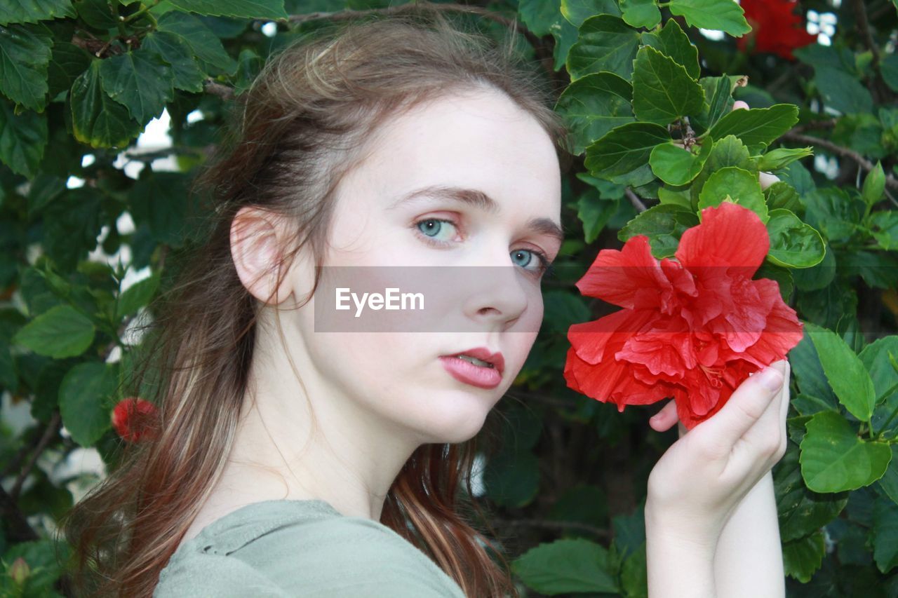 Close-up portrait of young woman holding red flower 