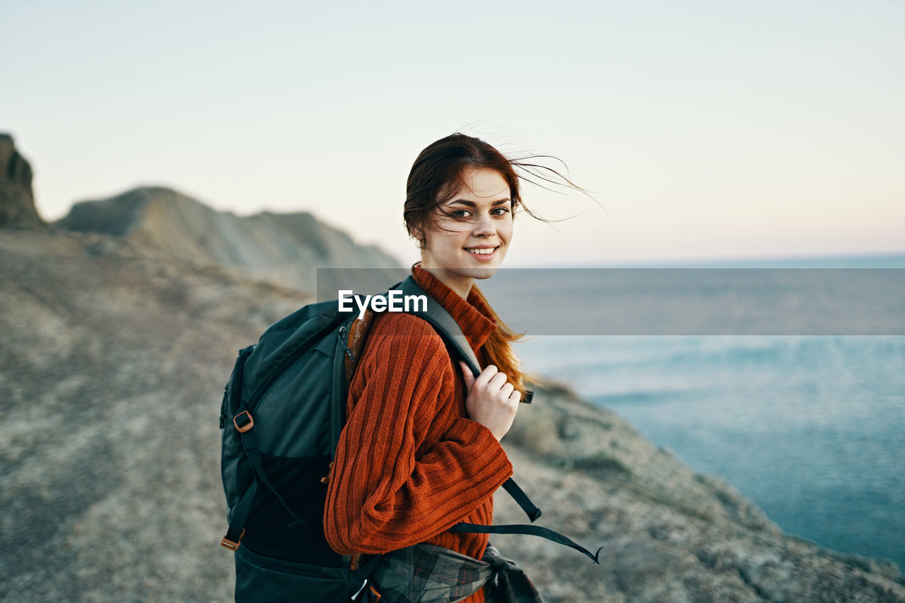 PORTRAIT OF SMILING YOUNG WOMAN STANDING ON BEACH