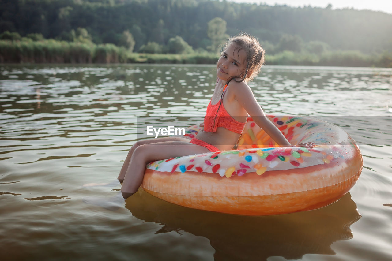 Girl swims with big donut inflatable ring on lake on hot summer day, happy summertime, cottagecore