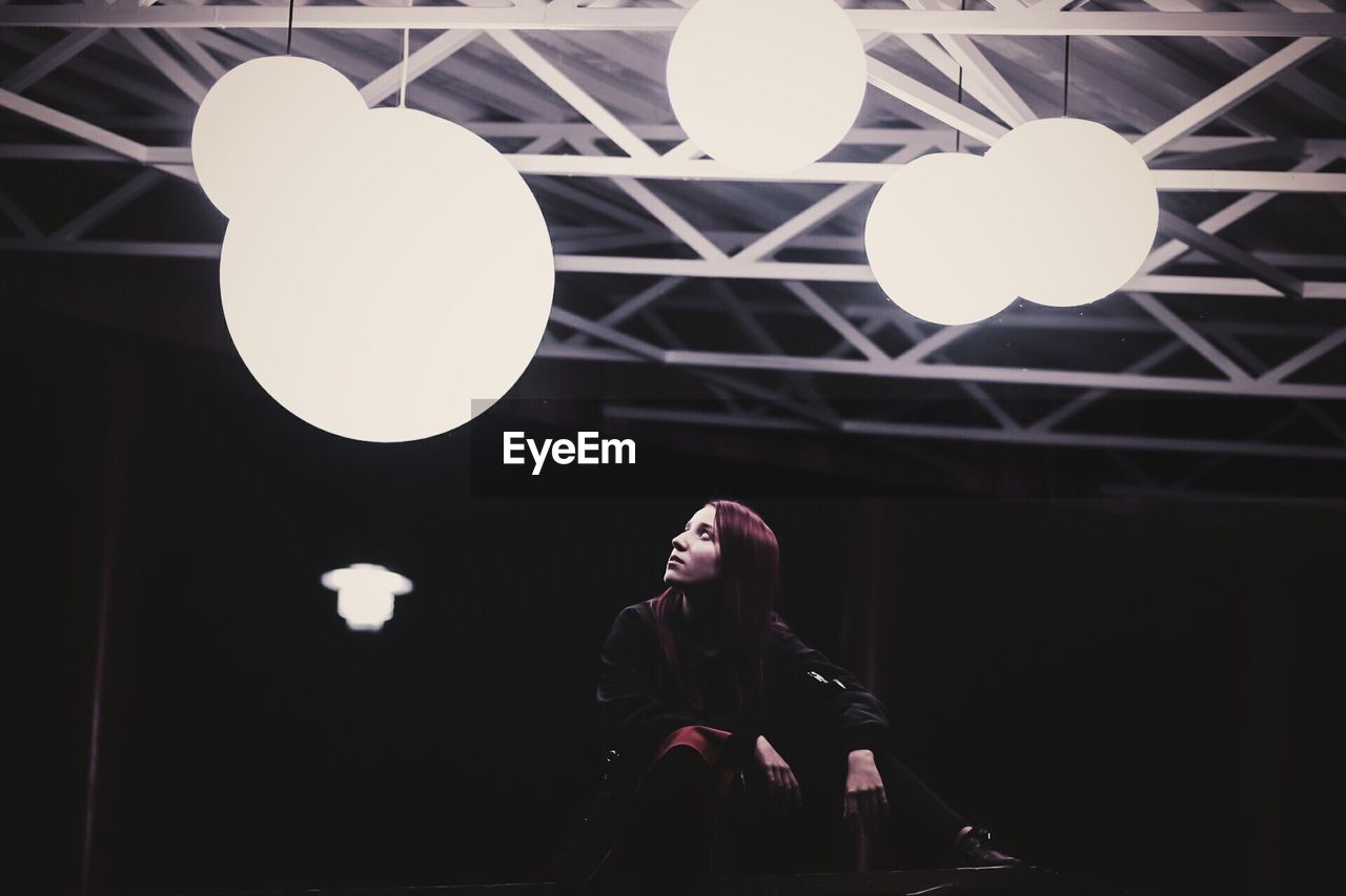 Woman looking at illuminated pendant lights in darkroom