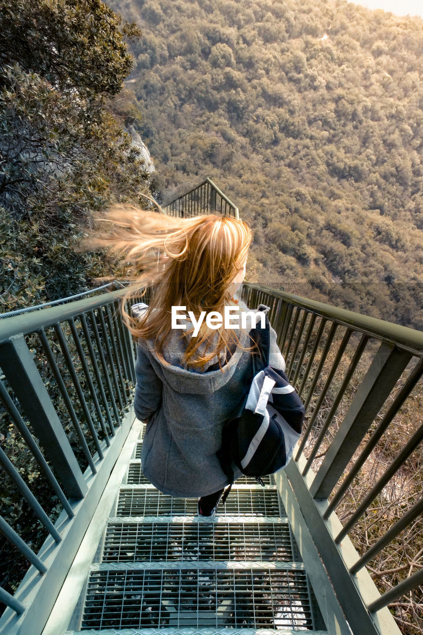 Rear view of woman moving down on steps against tree mountain