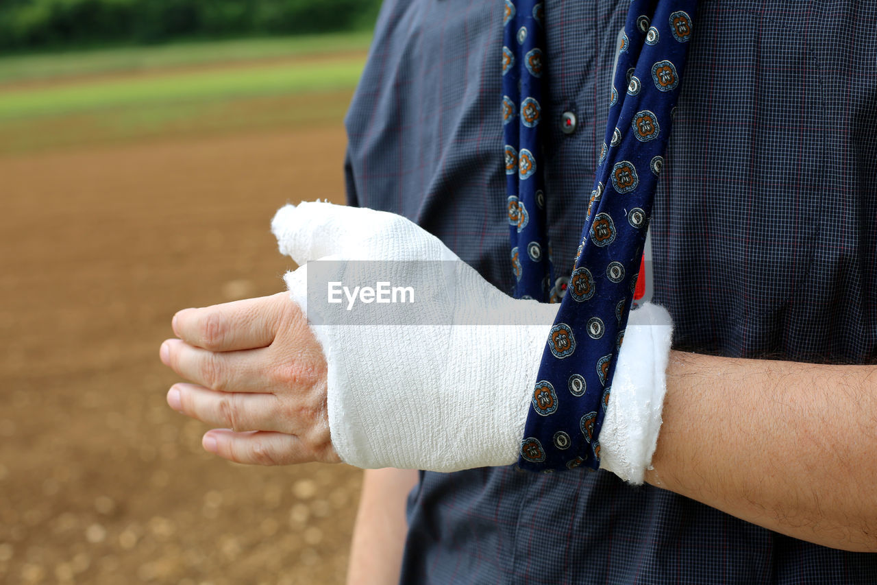 Midsection of man wearing bandage on injured hand while standing on land
