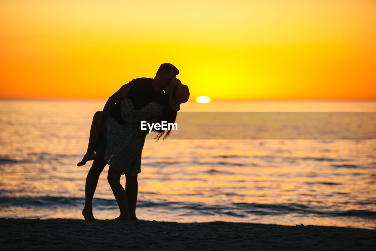 silhouette woman walking at beach against sky during sunset