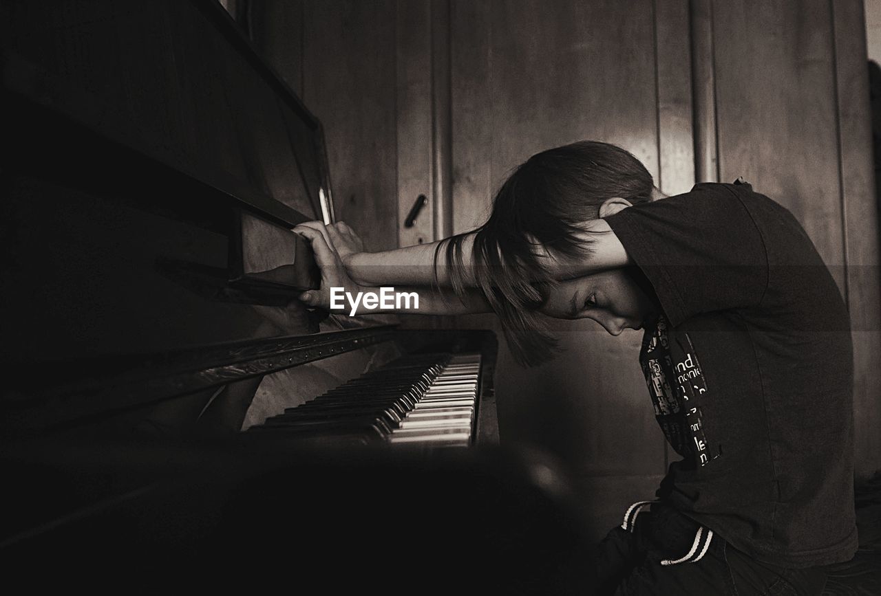 Side view of thoughtful boy sitting by piano at home