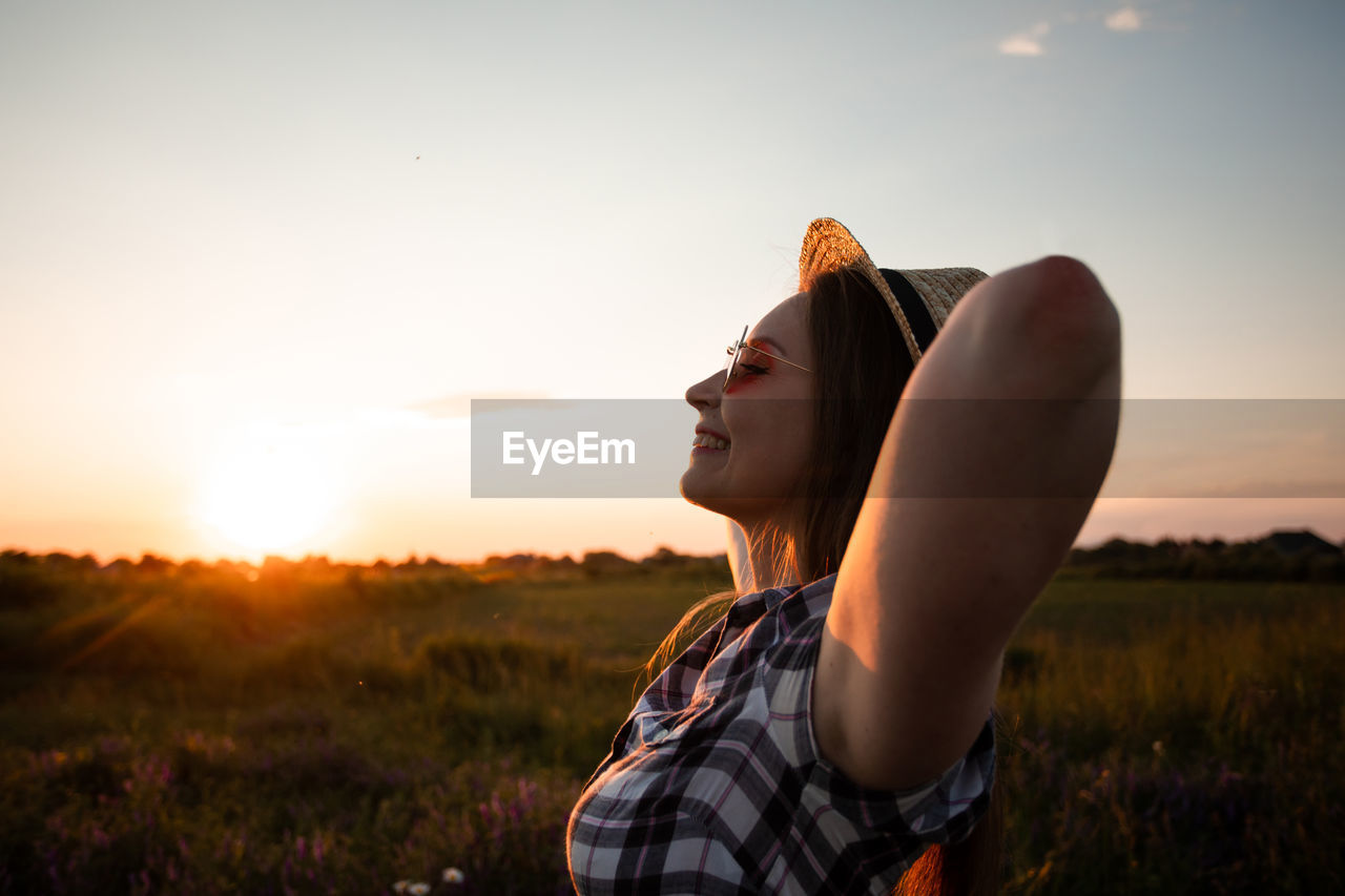 Young woman standing on land against sky during sunset