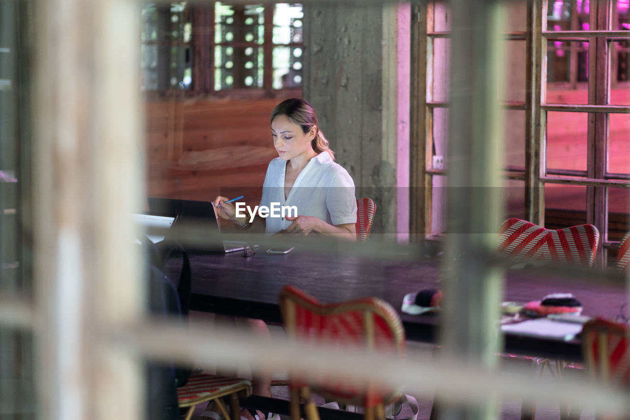 Concentrated enterprising businesswoman sits alone in office at large table with laptop