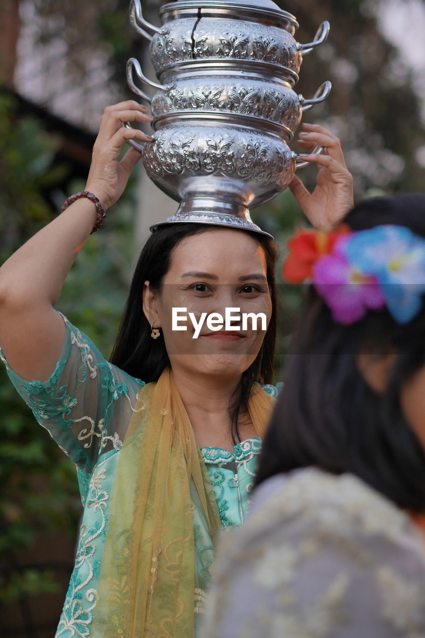 Portrait of smiling woman with face paint carrying stack containers on head during event