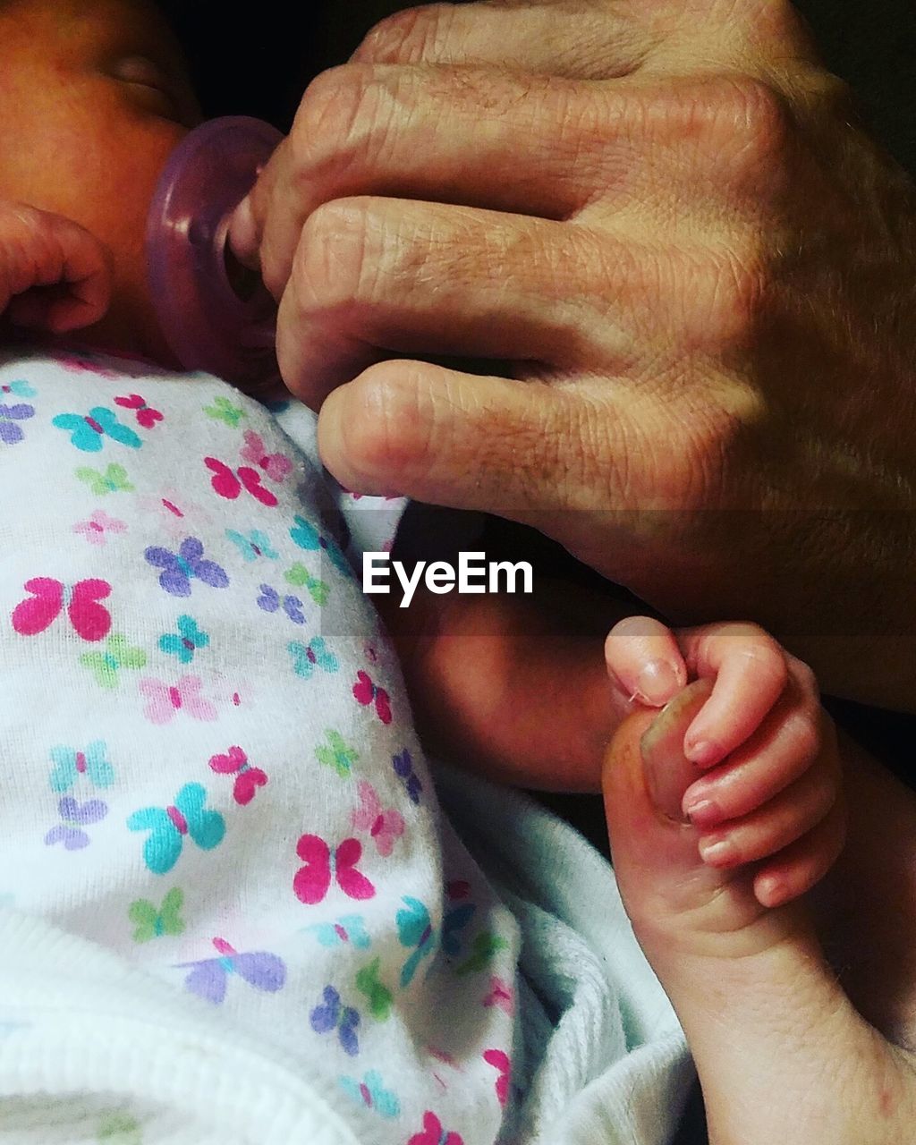 Cropped hand of parent putting pacifier in baby mouth