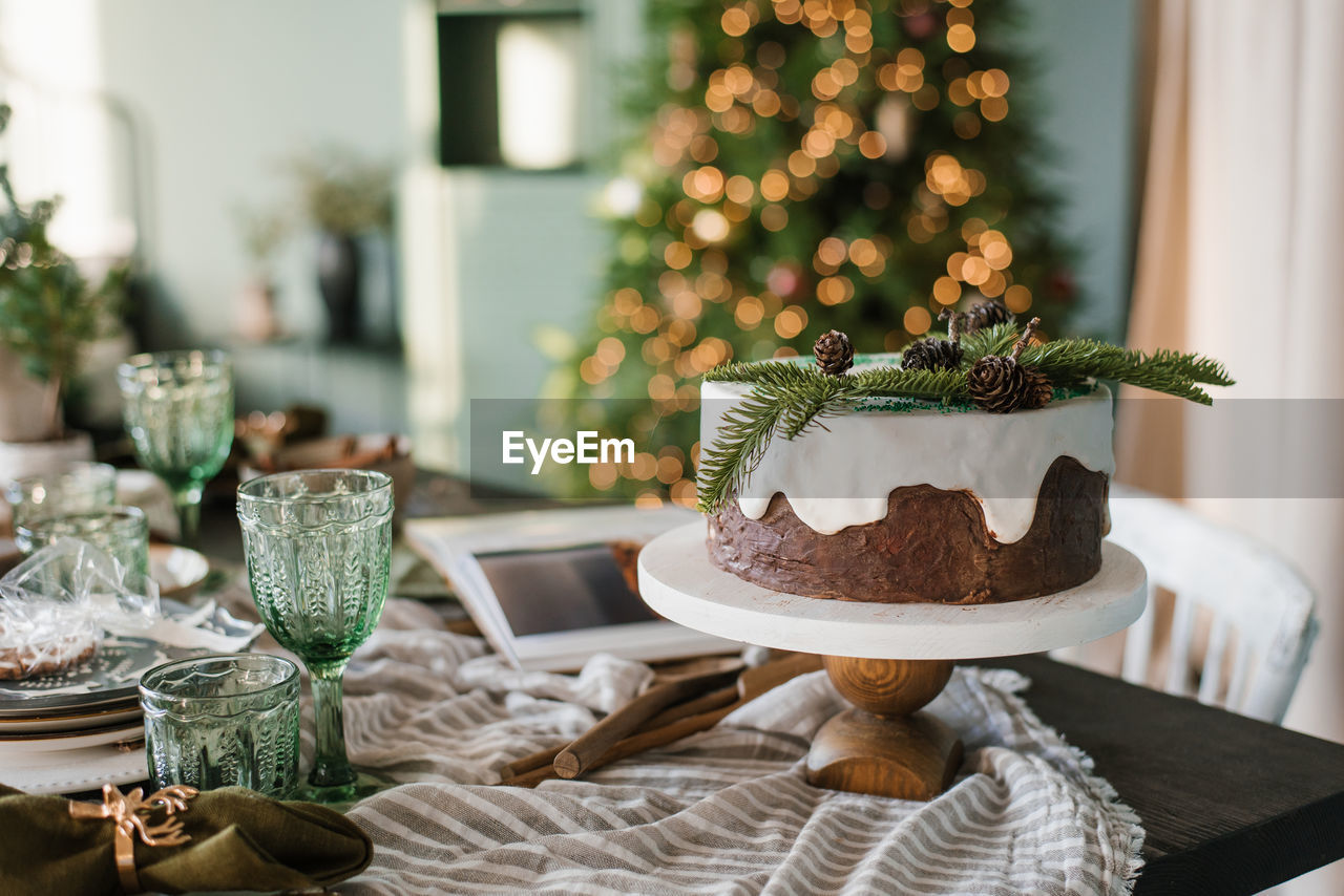 Festive christmas cake with white icing decorated with spruce branches stands on a set table against