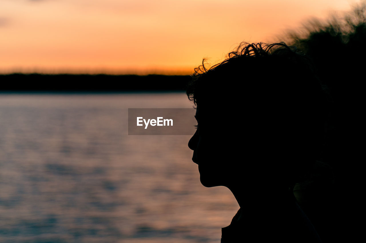 Close-up portrait of silhouette boy against lake during sunset