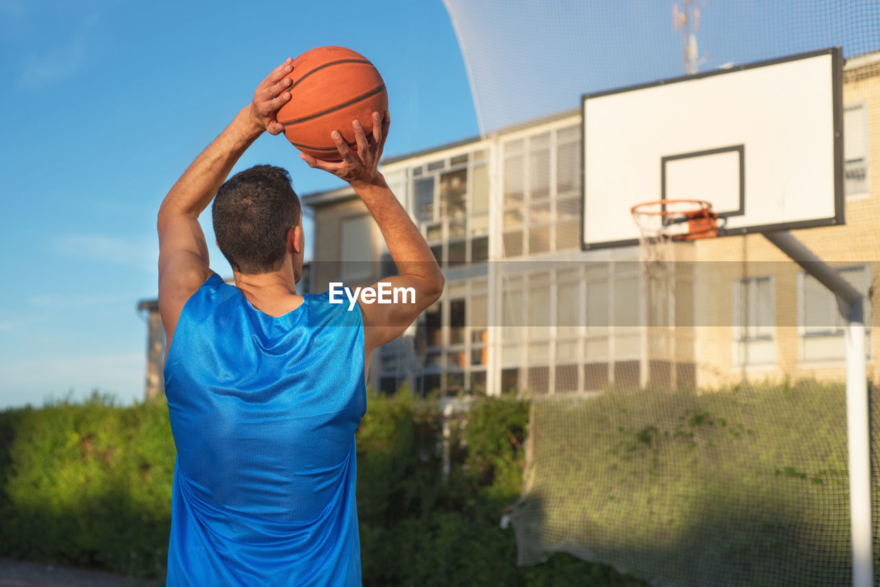 Low angle view of man playing basketball against blue sky