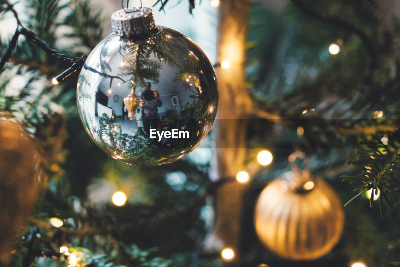 Close-up of man reflection on christmas decoration hanging on tree