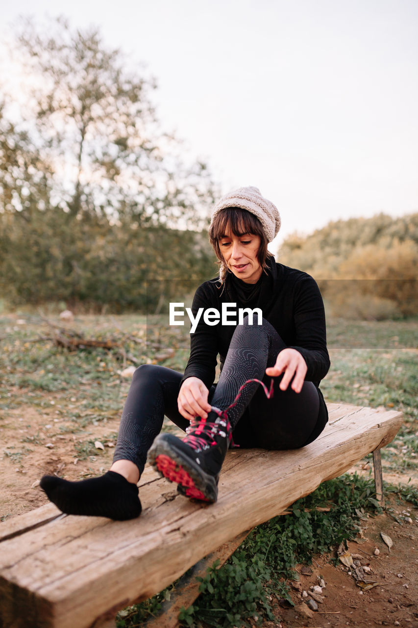 Full length of woman sitting on wooden bench at field