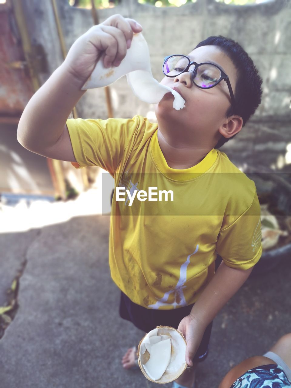 Full length of boy eating coconut while standing on footpath