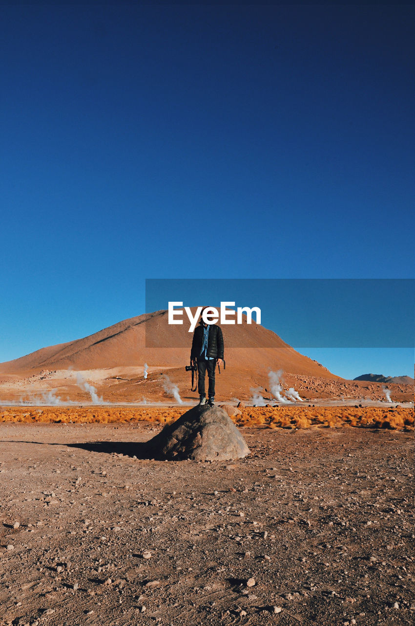 Full length of man standing on desert against clear blue sky