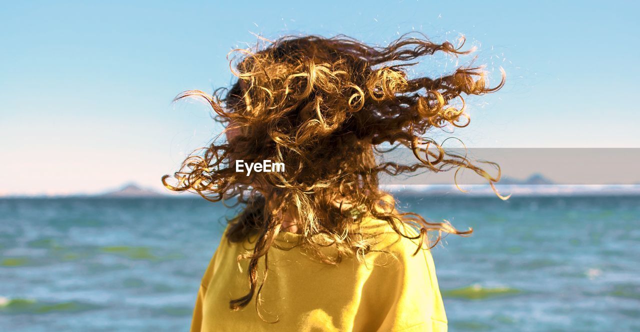 Woman shaking head while standing against sea