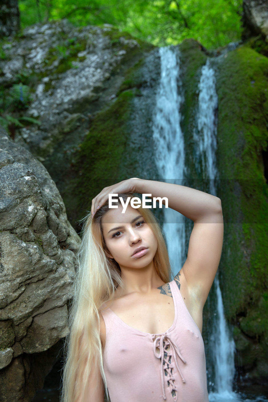 Portrait of beautiful young woman standing against waterfall