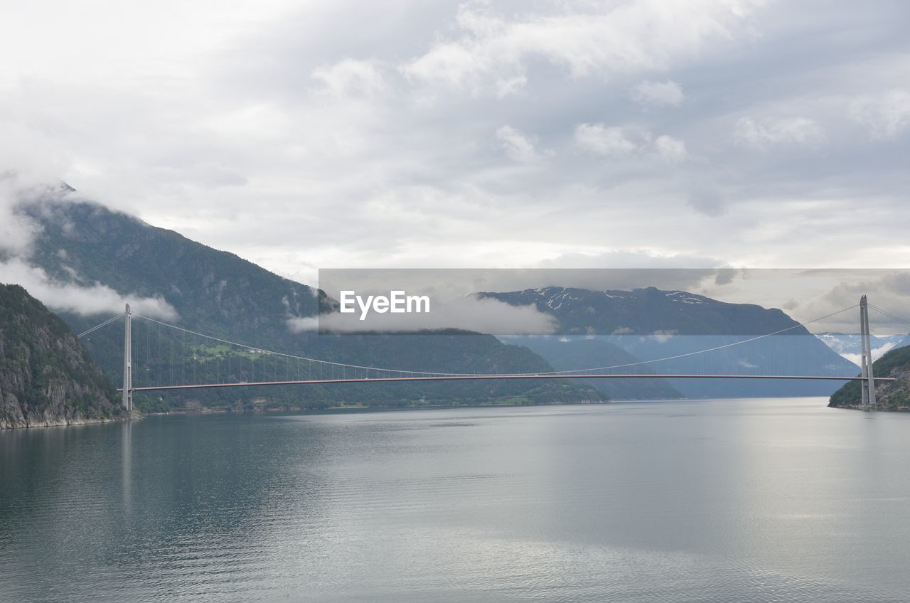 View of suspension bridge over river against cloudy sky