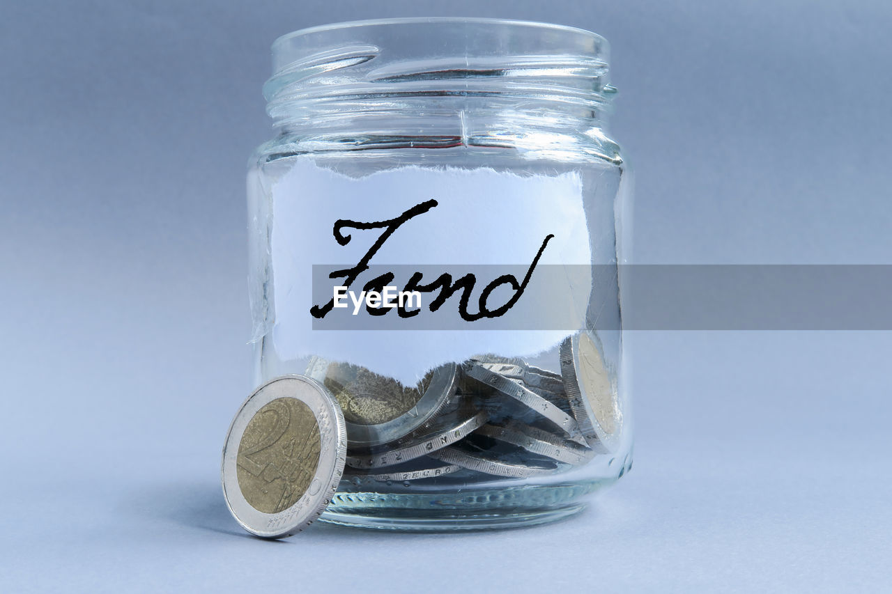 Close-up of coins in jar with fund text against gray background