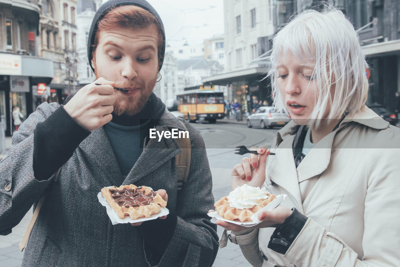 Belgium, antwerp, young couple eating belgian waffles on the street