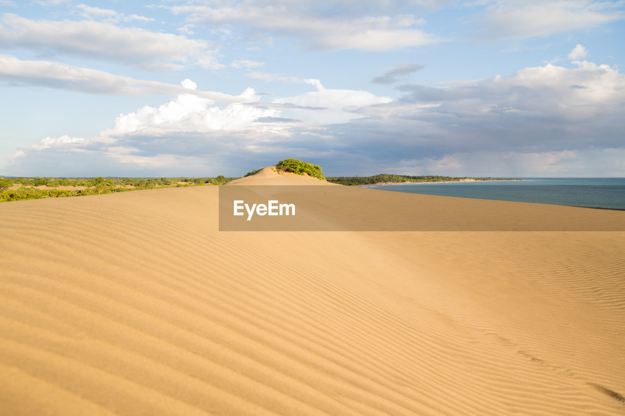 View of sand dunes in desert against cloudy sky