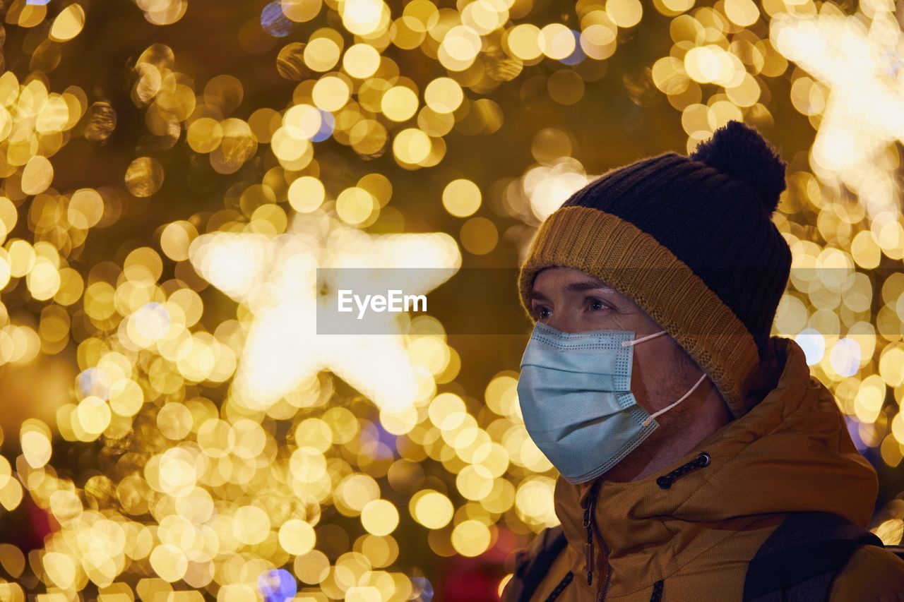Close-up of man wearing mask against illuminated christmas tree during winter