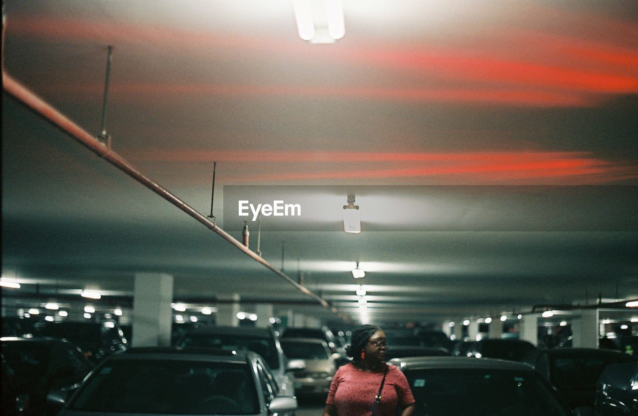 REAR VIEW OF WOMAN MOVING IN ILLUMINATED PARKING LOT