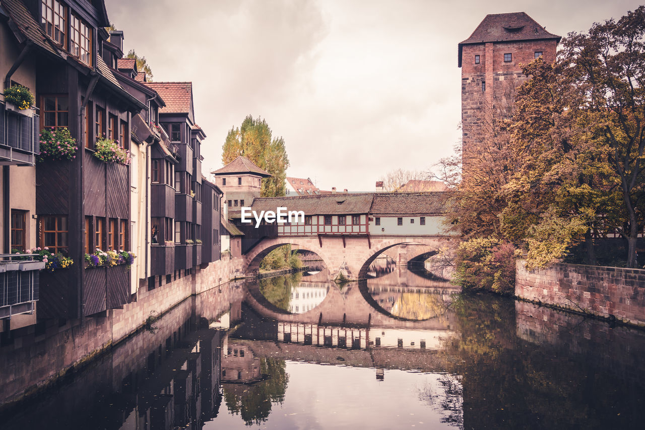 Bridge over river by buildings against sky