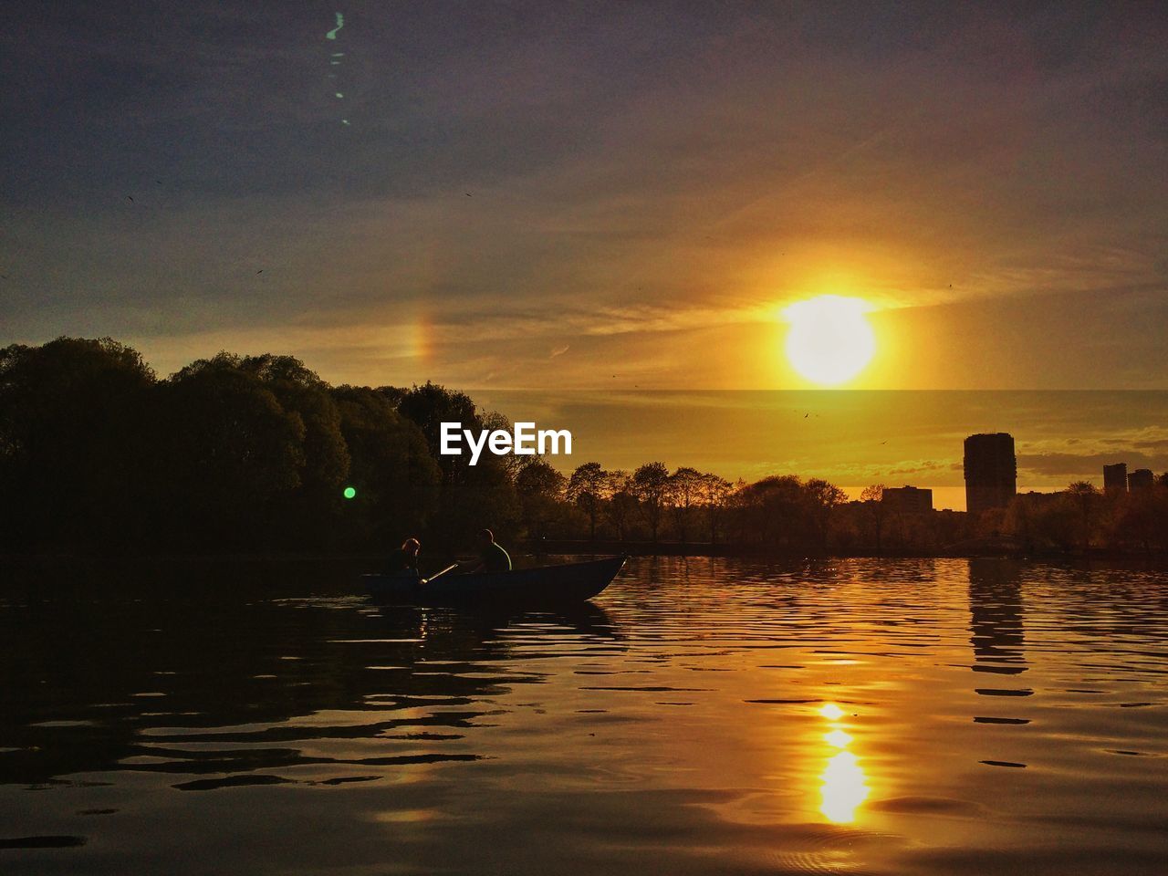 People on boat in lake against orange sky during sunset