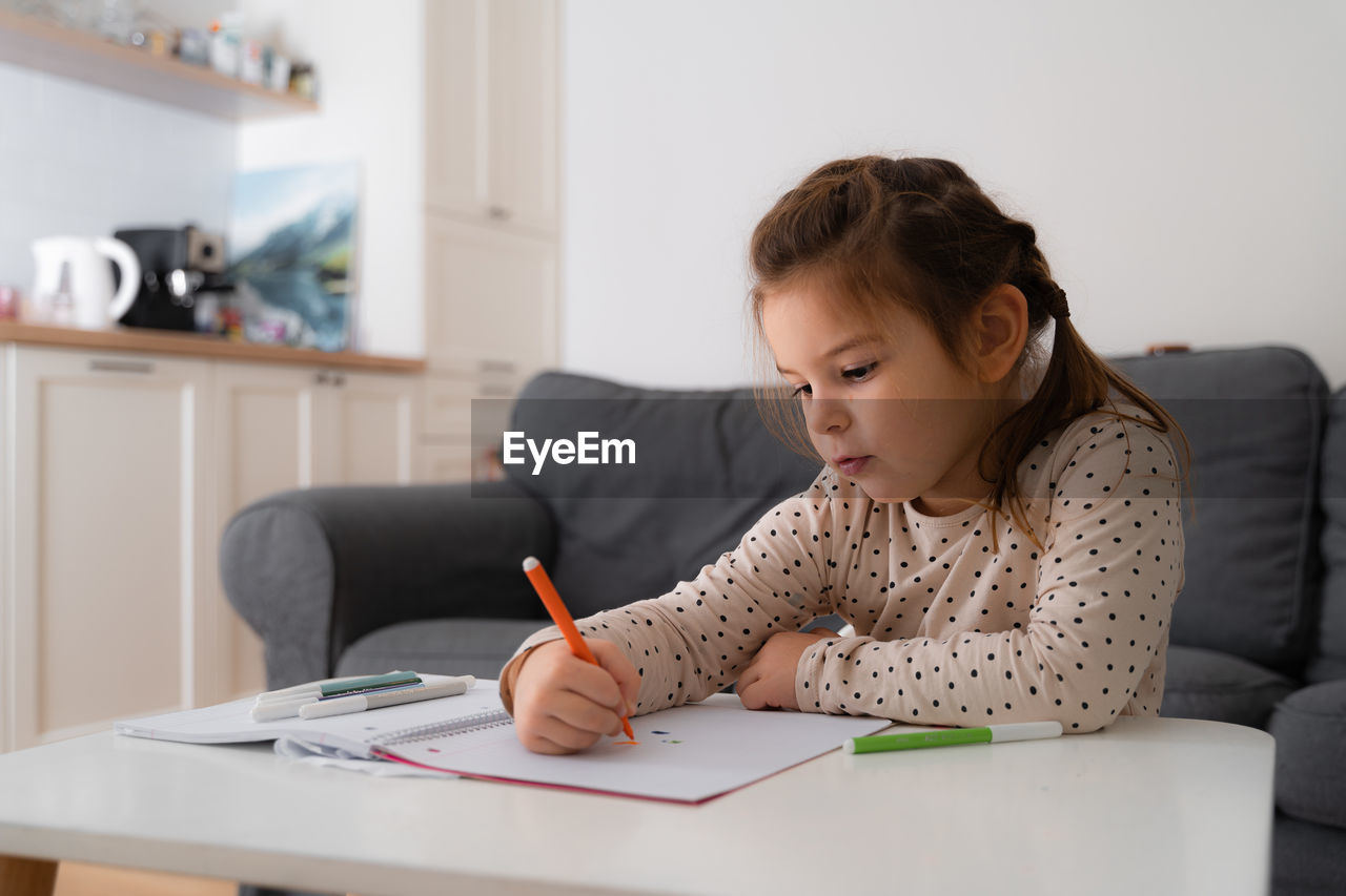 Portrait of cute preschooler child girl drawing with pencils at home 