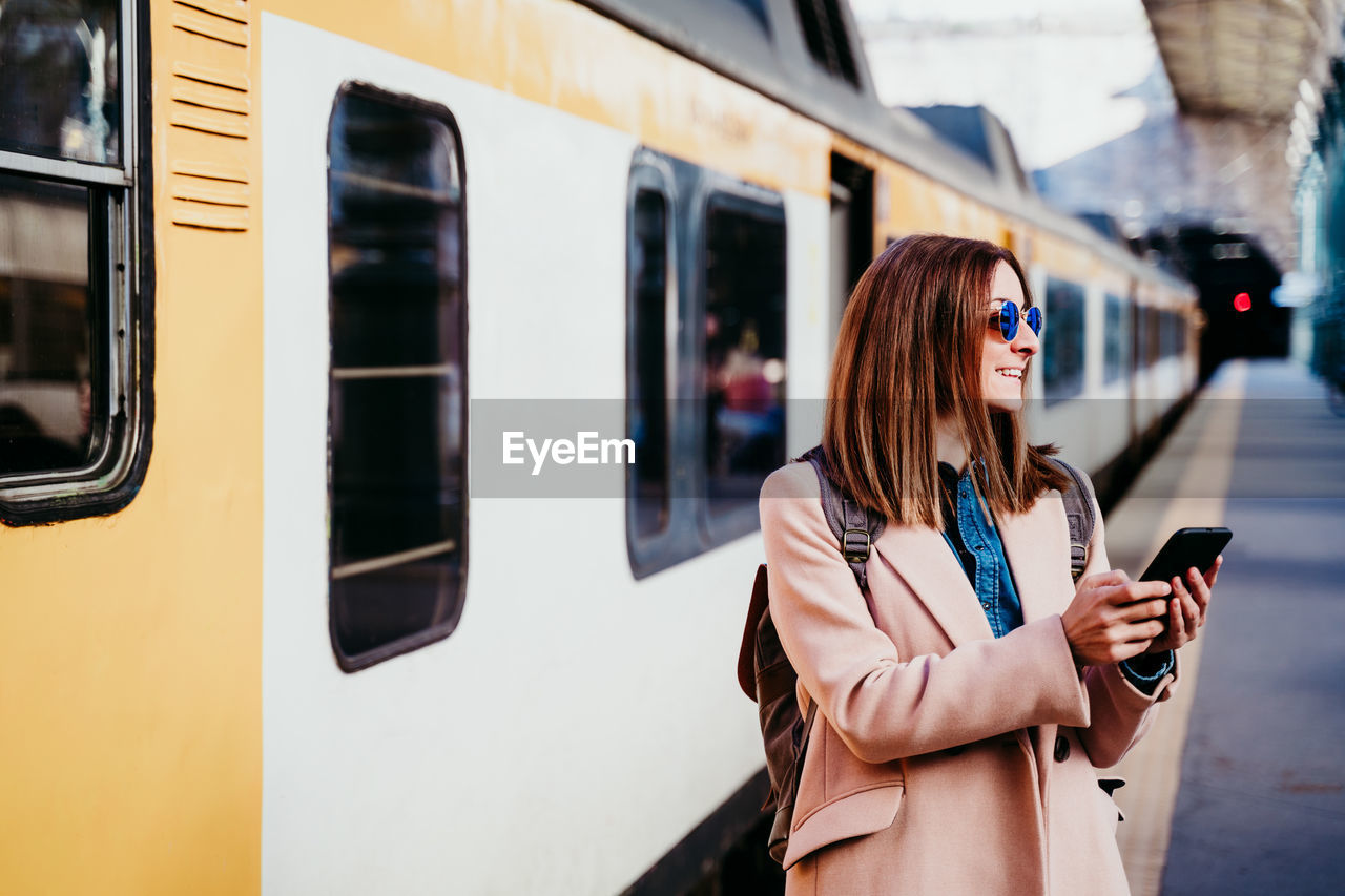 Woman with phone standing by train on railroad station platform