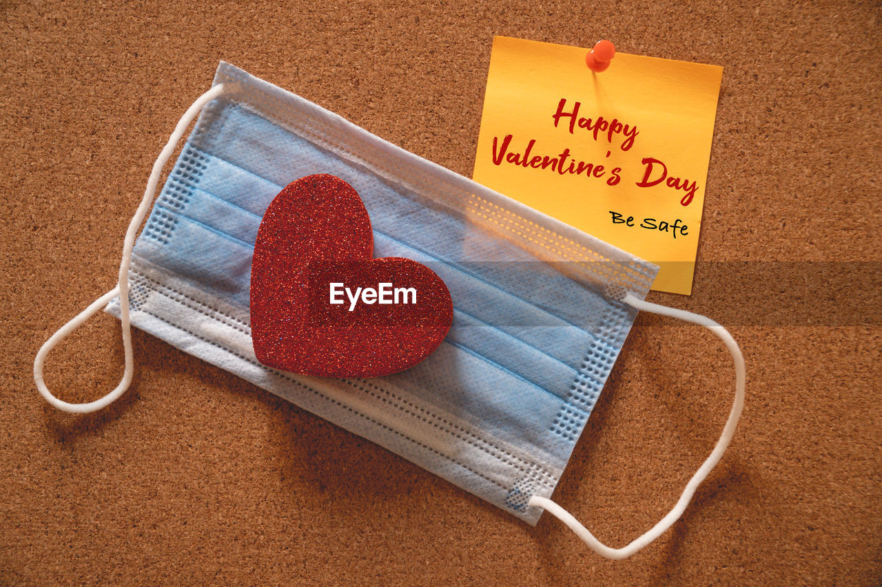 Top view of a heart shape and a face mask with happy valentine's day and be safe note