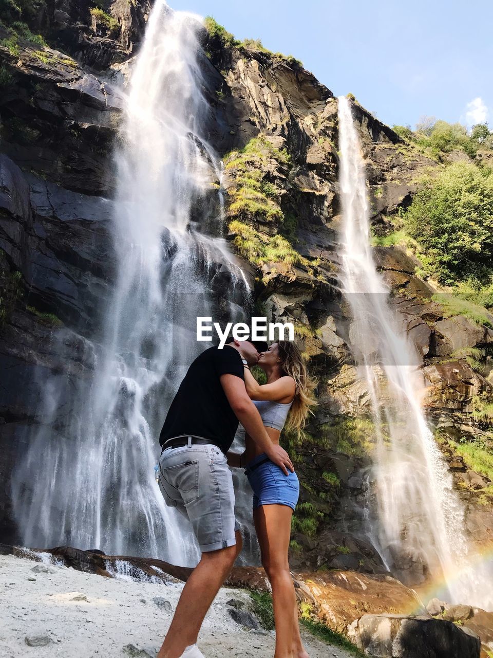 Side view of couple kissing while standing against waterfall