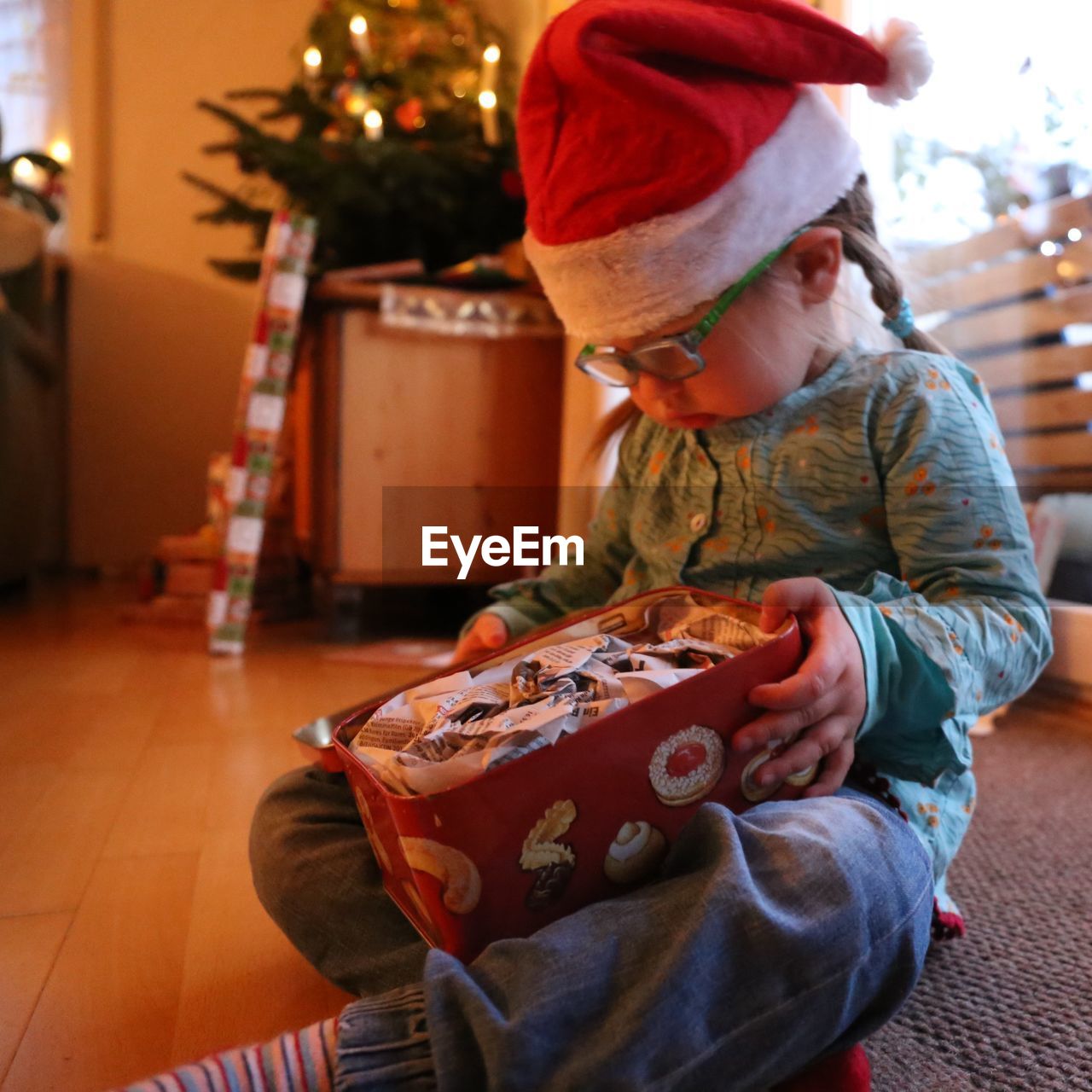 Cute girl wearing santa hat holding container while sitting at home