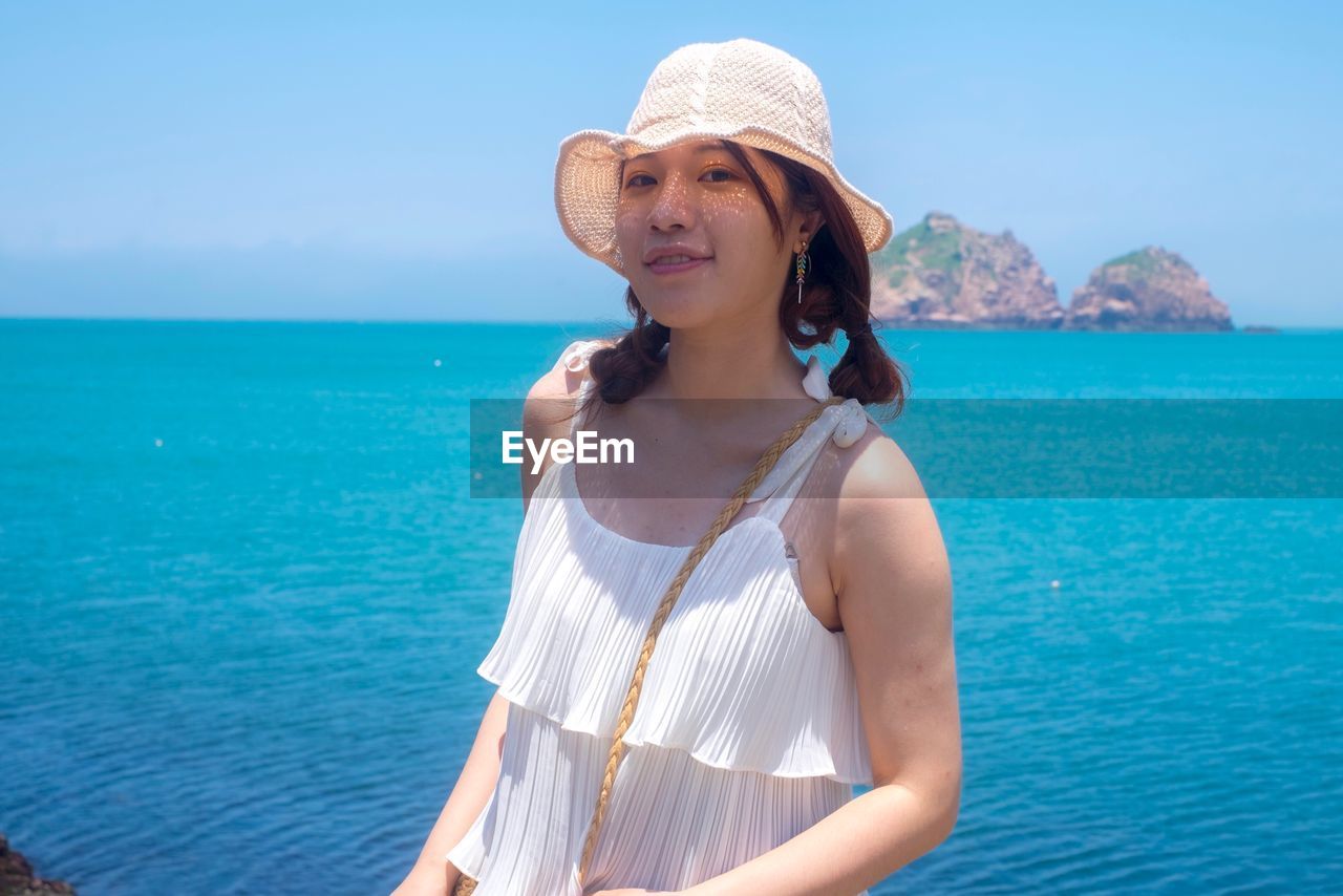 Portrait of beautiful young woman standing against blue sea