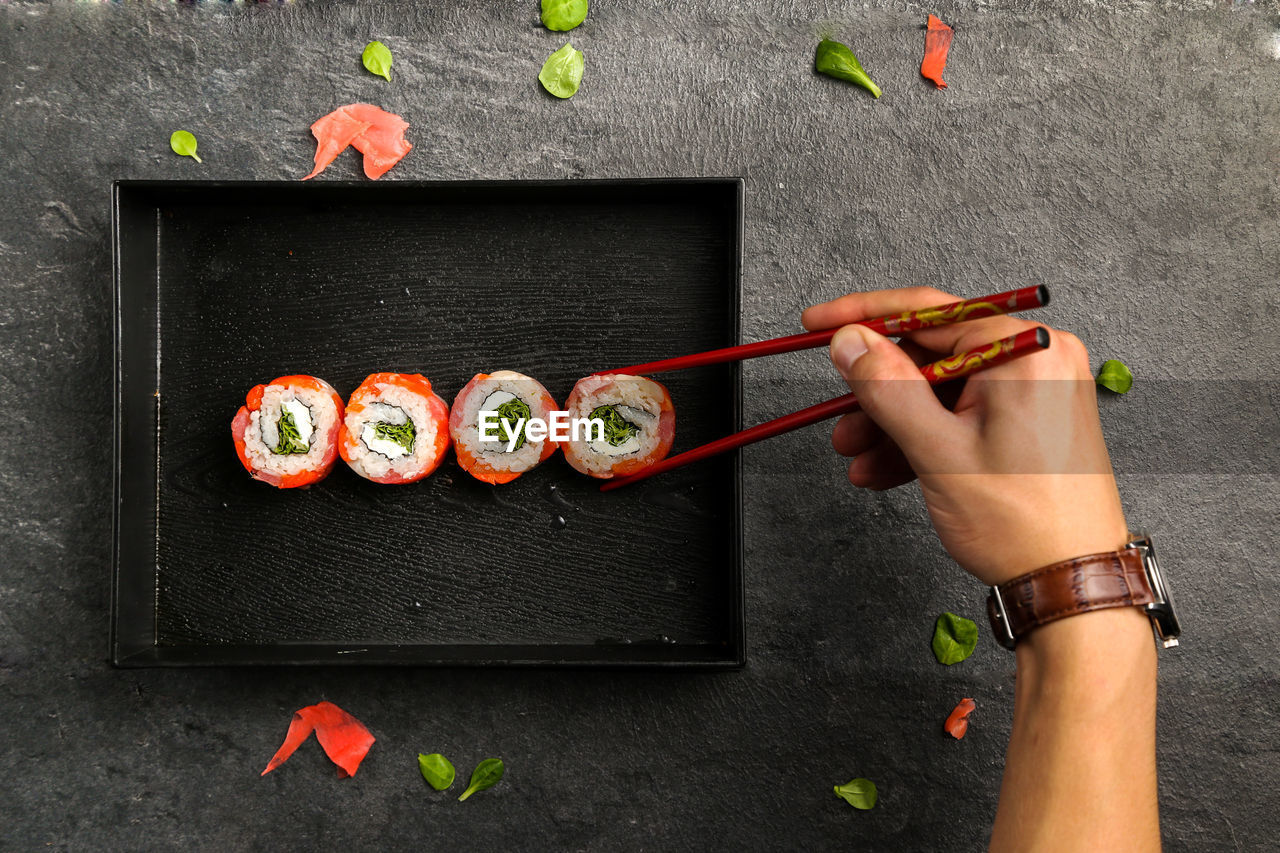 Cropped image of man holding sushi with chopsticks in plate