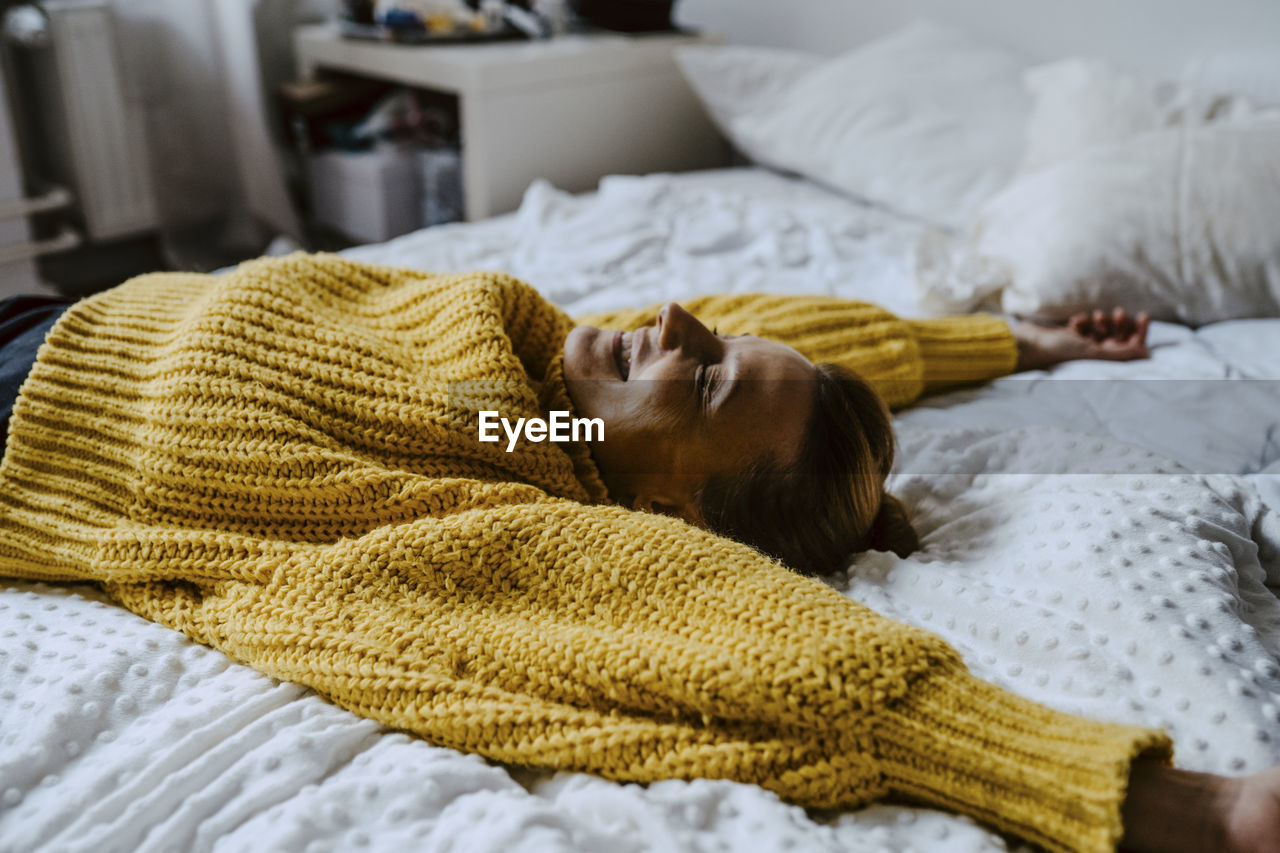 Woman with hand raised lying on bed at home