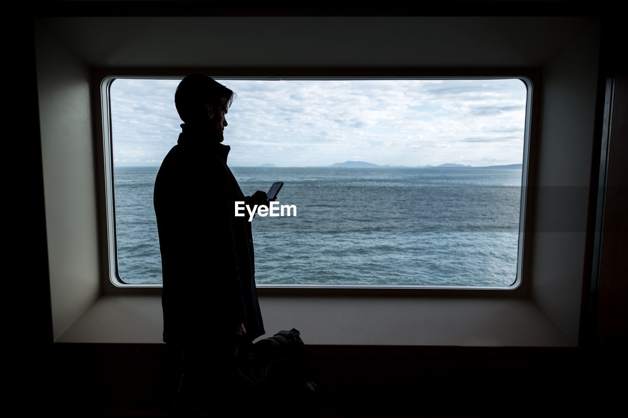 Man using phone against window at sea