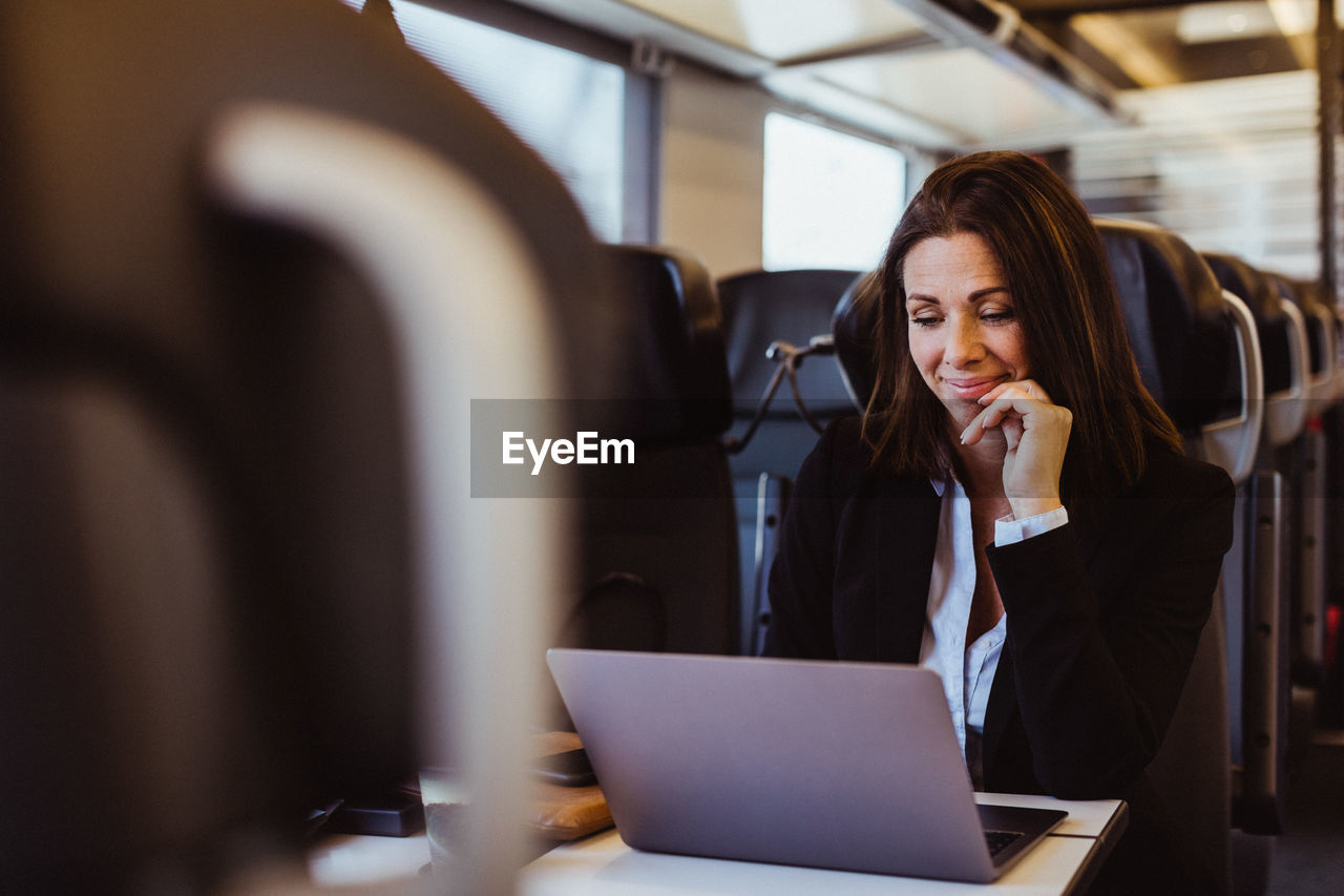 Smiling businesswoman using laptop while sitting in train