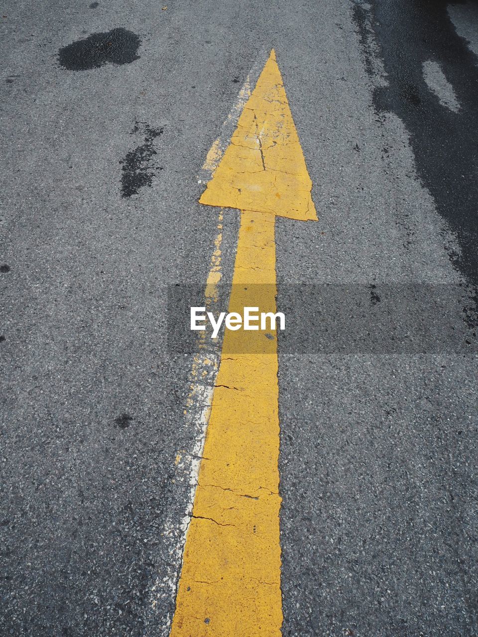 HIGH ANGLE VIEW OF YELLOW ARROW SYMBOL ON ROAD