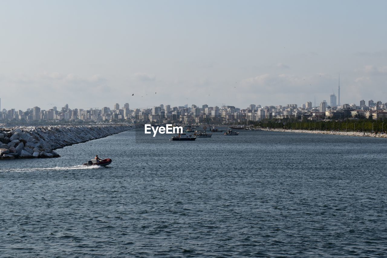 BOATS IN SEA BY BUILDINGS AGAINST SKY