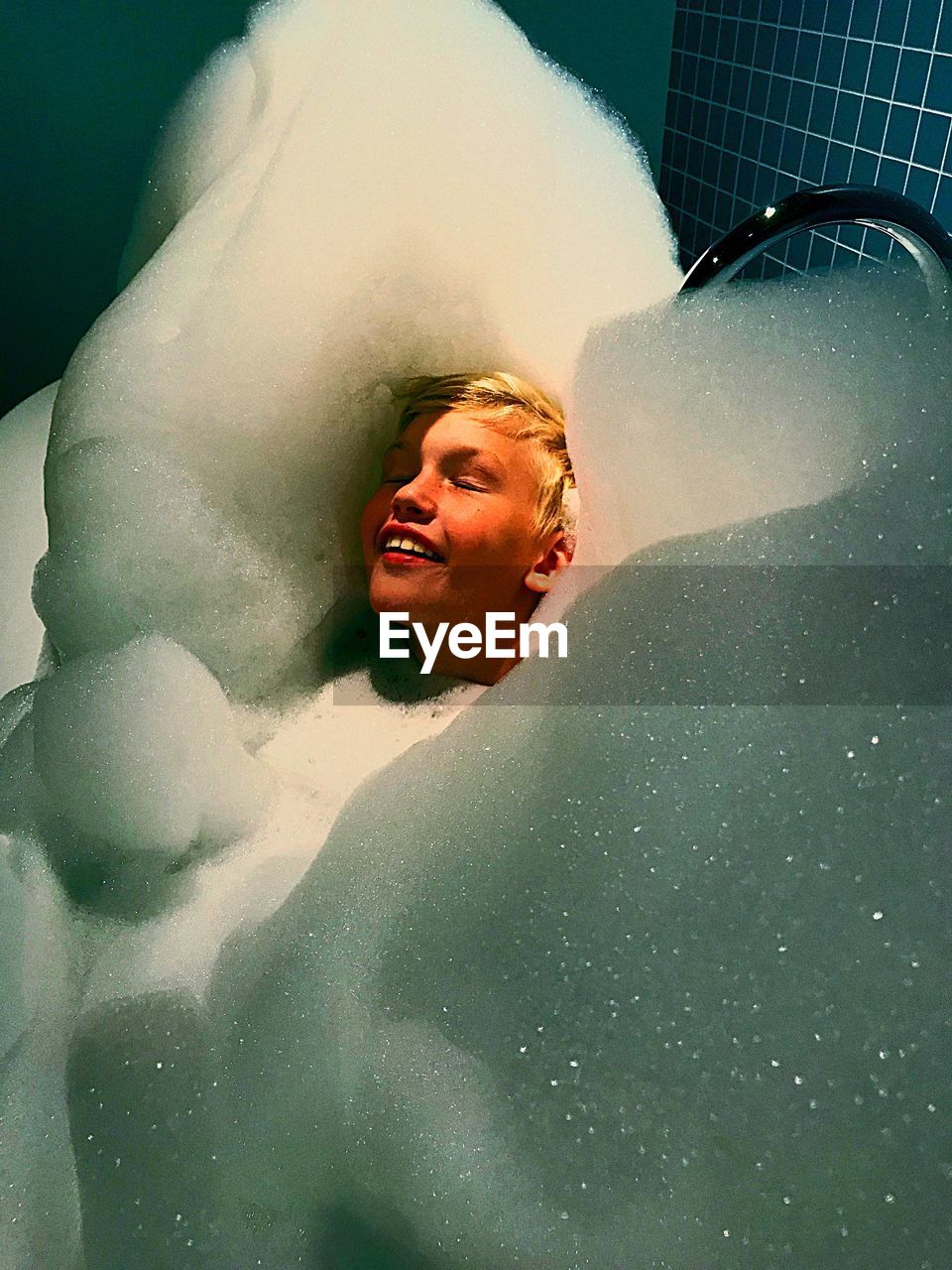 High angle view of smiling boy with eyes closed sitting in bathtub