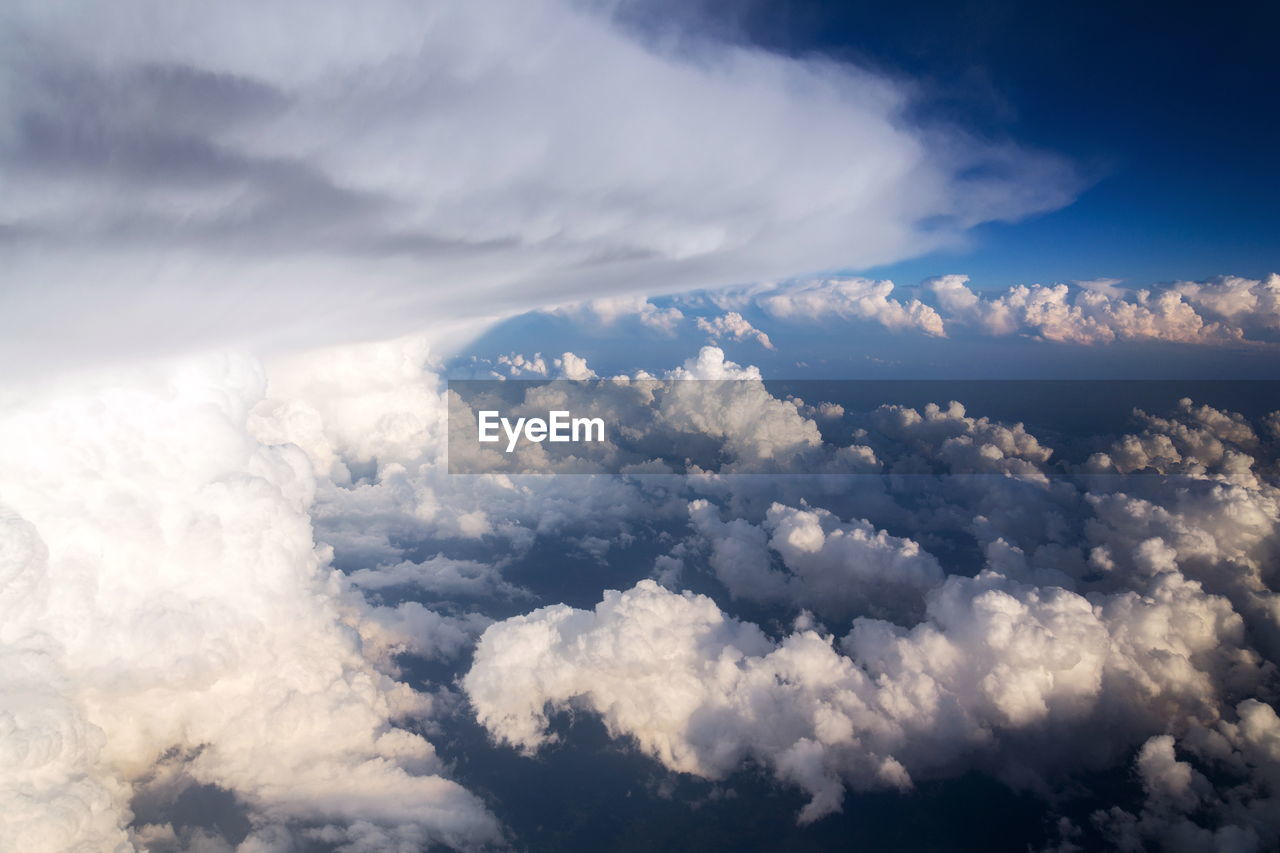 sky, cloud, cloudscape, environment, nature, beauty in nature, aerial view, scenics - nature, landscape, dramatic sky, blue, atmosphere, no people, outdoors, wind, horizon, backgrounds, overcast, storm cloud, high up, airplane, idyllic, mountain, sunlight, daytime, white, tranquility, fluffy, high angle view, travel, flying, storm, day, above, air vehicle