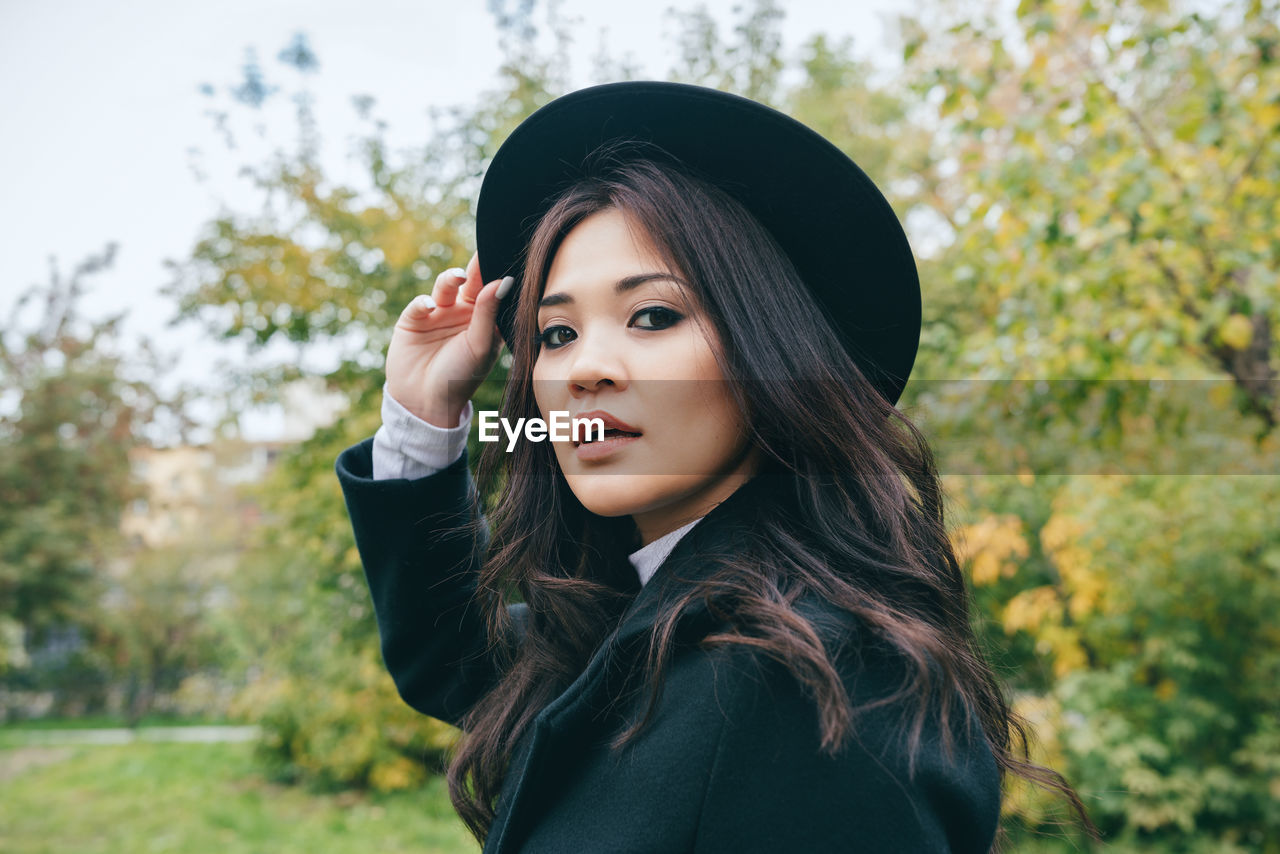 Portrait of beautiful young woman standing against trees