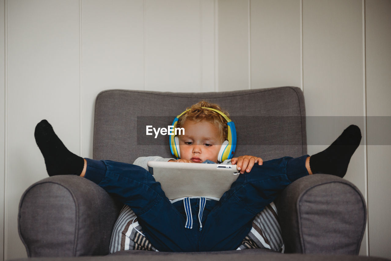 Child inside during isolation playing with tablet feet up on couch