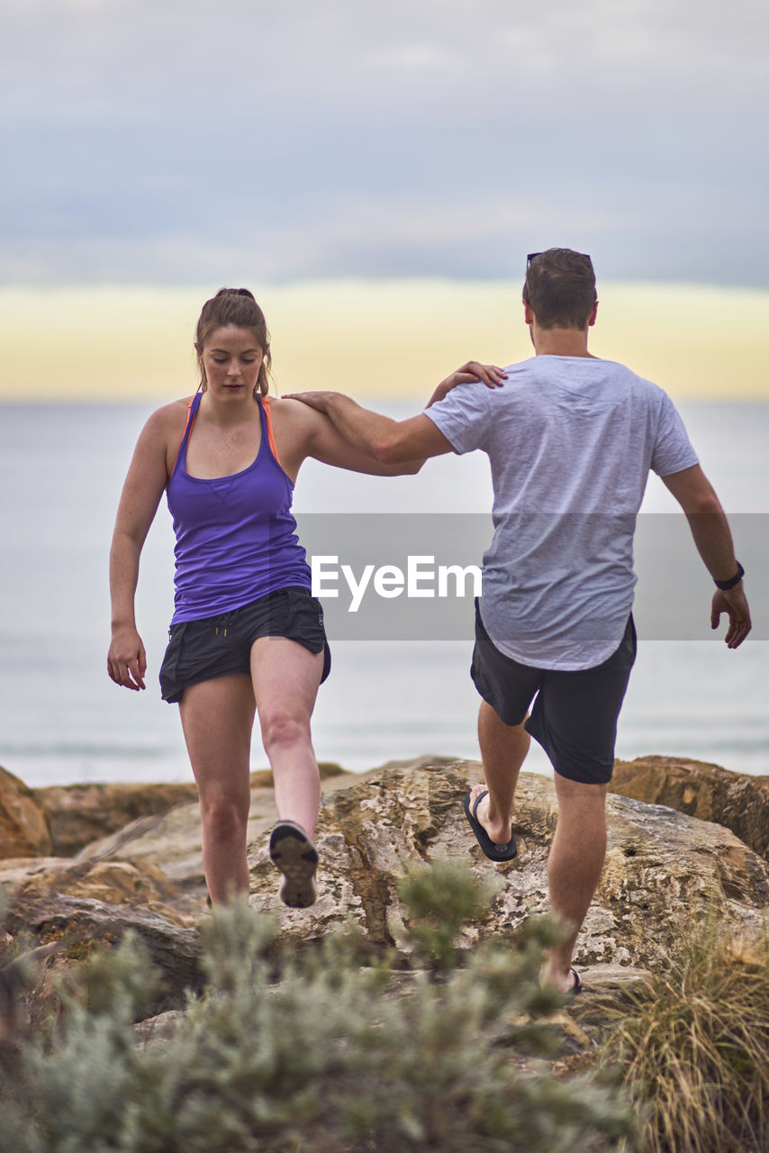 Young woman exercising with fitness instructor at beach