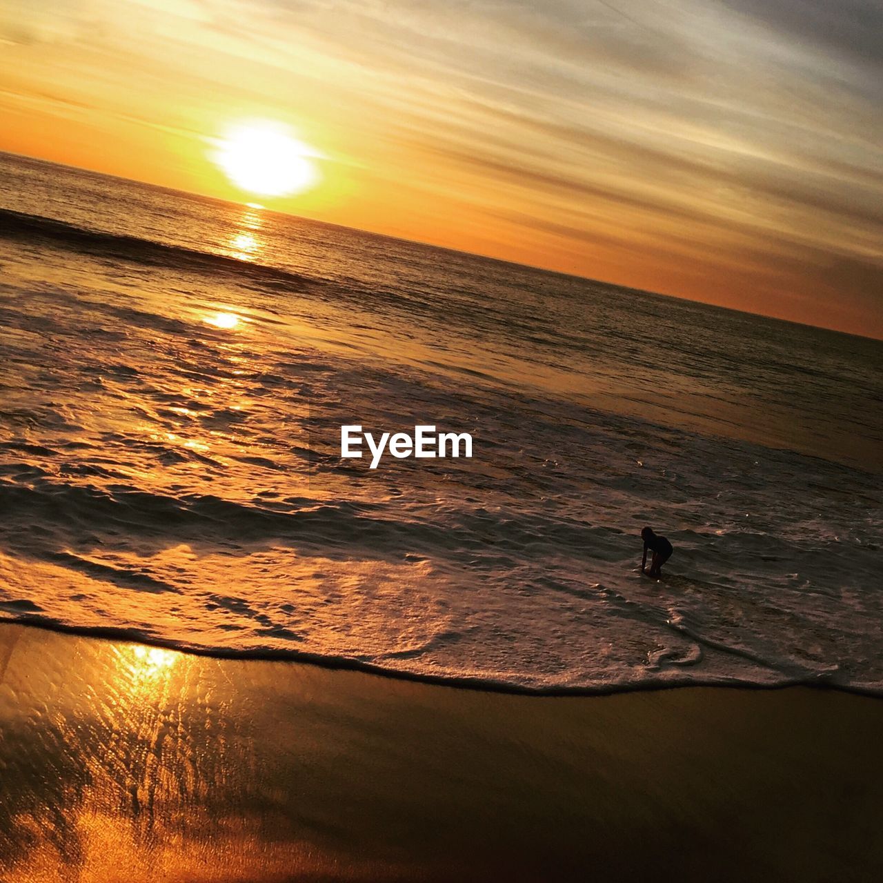 Tilt shot of girl on shore in sea against orange sky during sunset