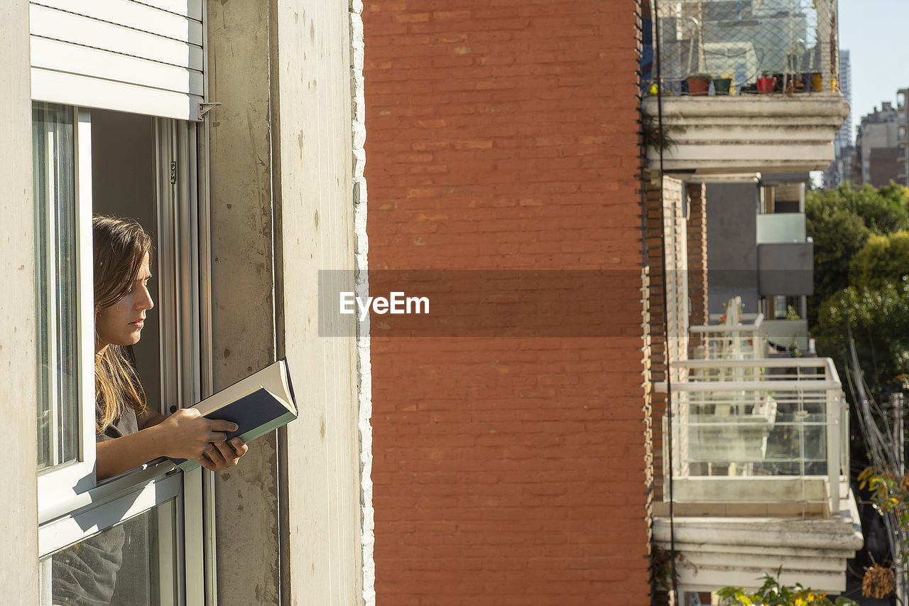 Woman in the windows during quarantine reading a book